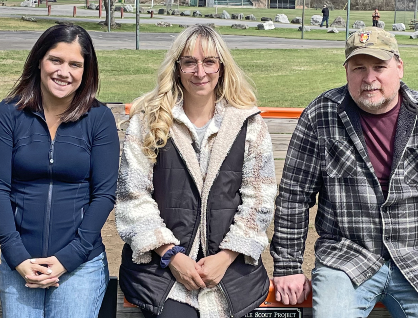 WEIC board members Two women and one man sit on a fence in a community park
